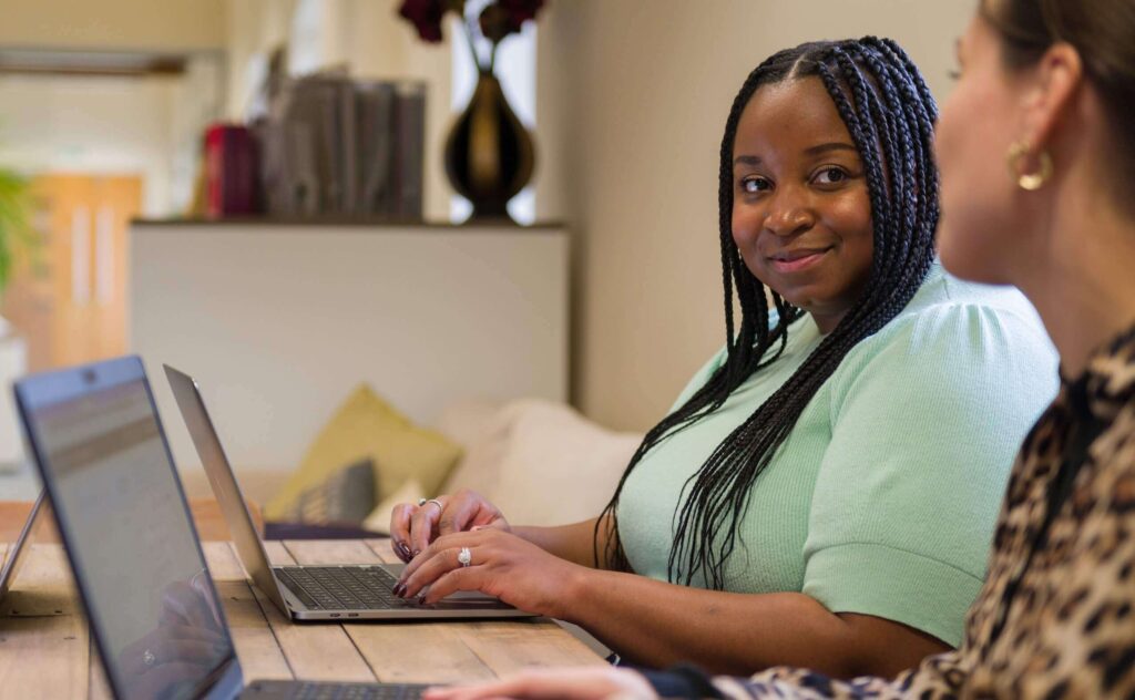 Friendly women in green top on laptop talking to colleague